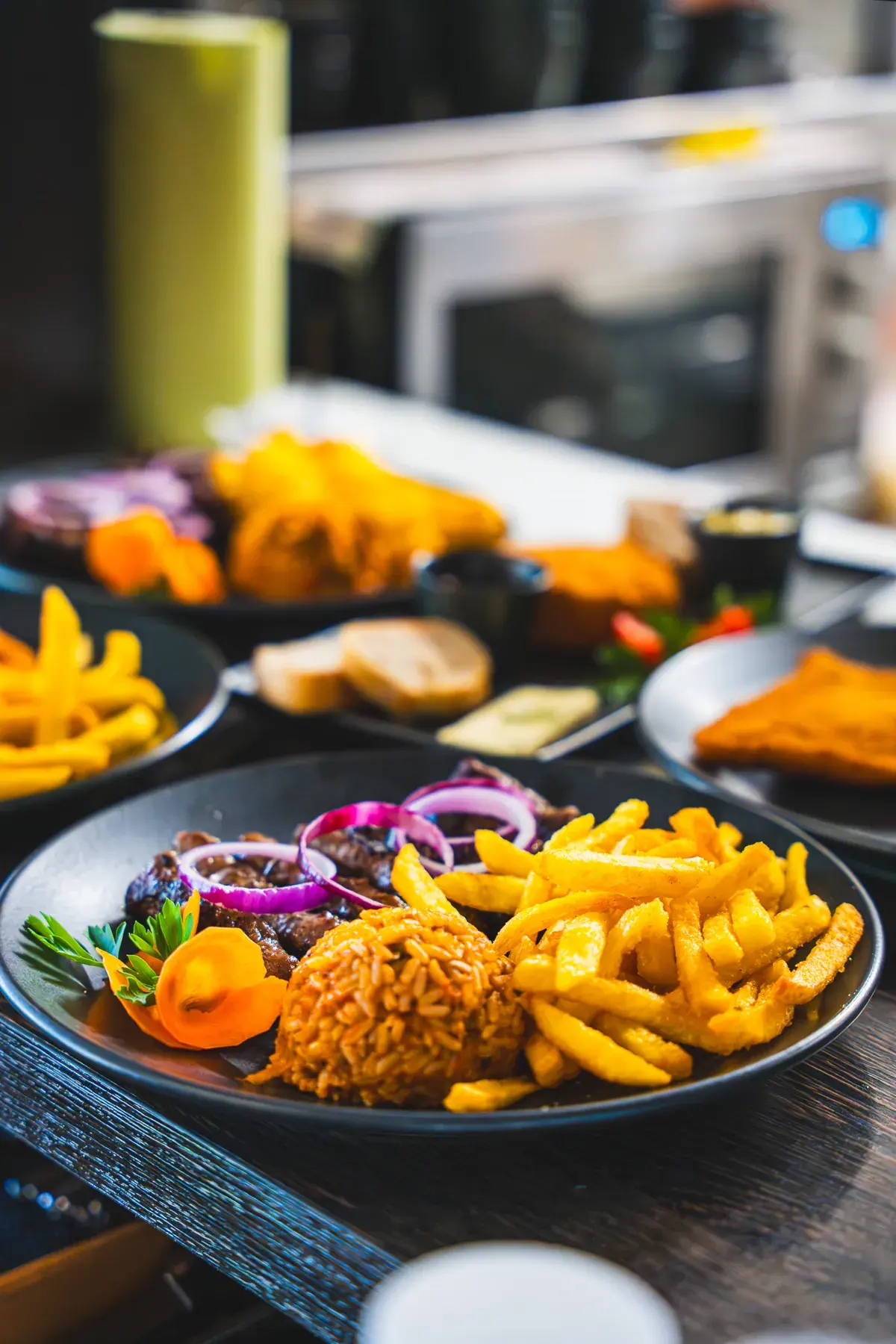 Cevapcici mit roten Zwiebeln, Pommes frites und Djuwetschreis auf dunklem Teller