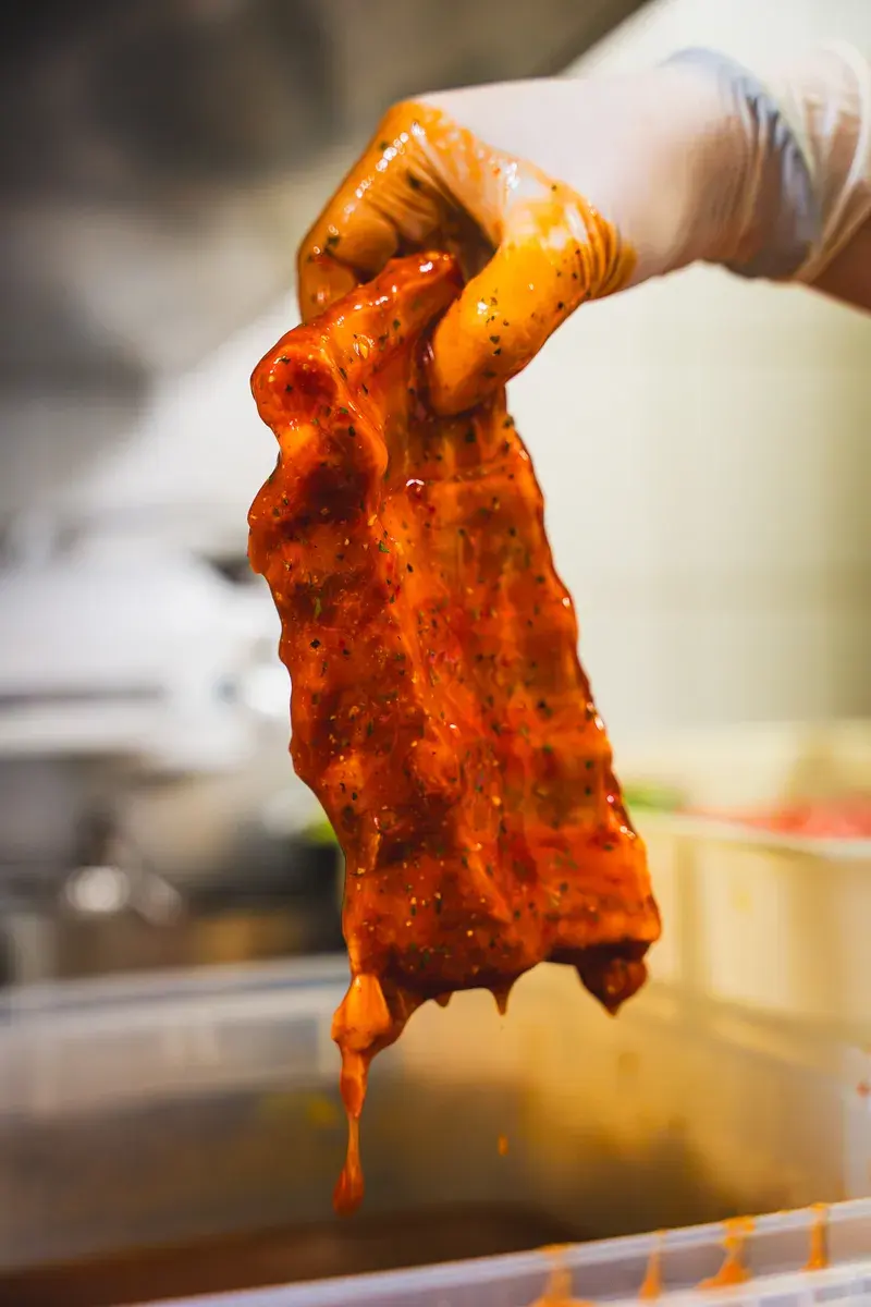 Eine marinierte Rippe, mit Handschuh hochgehalten, die Marinade tropft