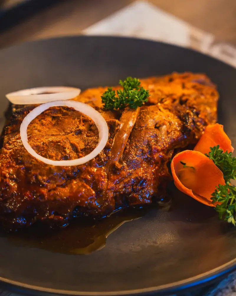 Angerichtete Spareribs mit Zwiebelring und Karottenblume