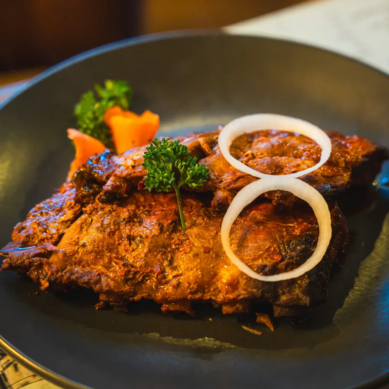 Spareribs mit dunkler Glasur auf dem Teller, obenauf zwei Zwiebelringe und Petersilie