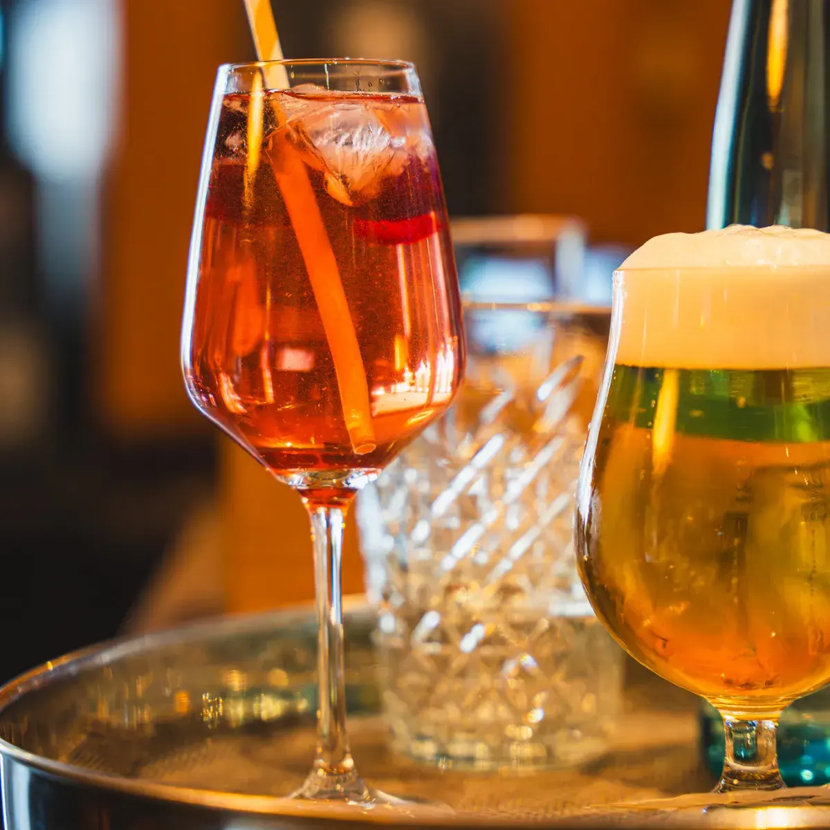Aperol Spritz mit Strohhalm und frisch gezapftes Bier mit Schaumkrone auf einem Tablett am Tresen
